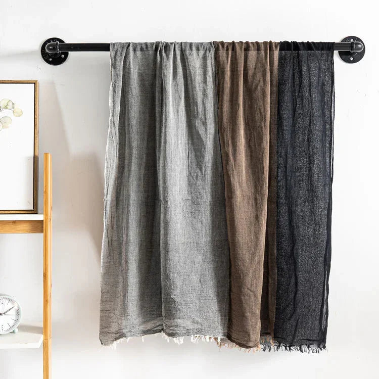 Three linen curtains in gray, brown, and black hanging on a black industrial curtain rod on white wall