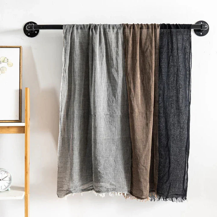Three linen curtains in gray, brown, and black hanging on a black industrial curtain rod on white wall