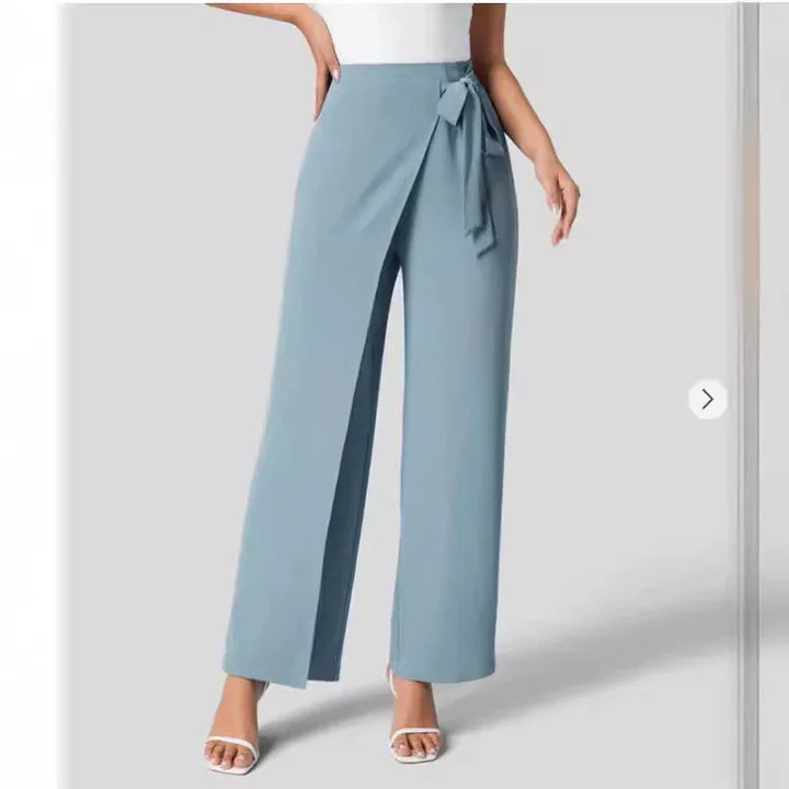 Woman wearing light blue wrap pants with side tie and white sandals against gray background