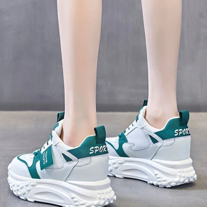 White and green chunky sport sneakers with textured soles worn by a person on a gray floor