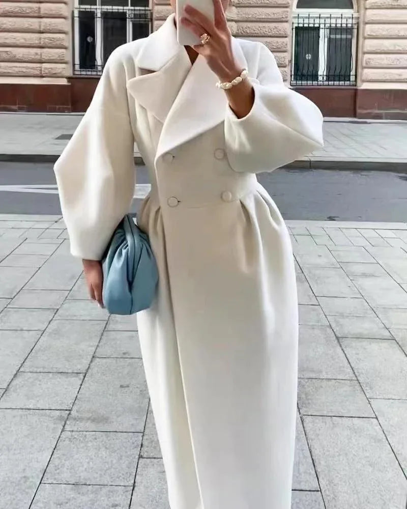 Woman in stylish white long coat with puff sleeves holding blue handbag and taking a mirror selfie outdoors