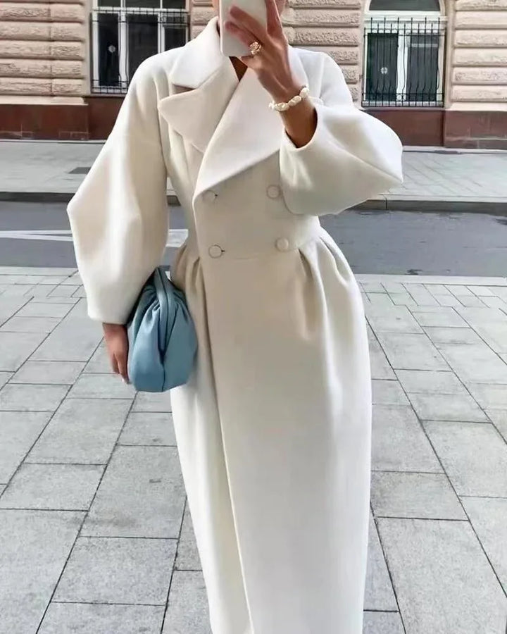 Woman in stylish white long coat with puff sleeves holding blue handbag and taking a mirror selfie outdoors