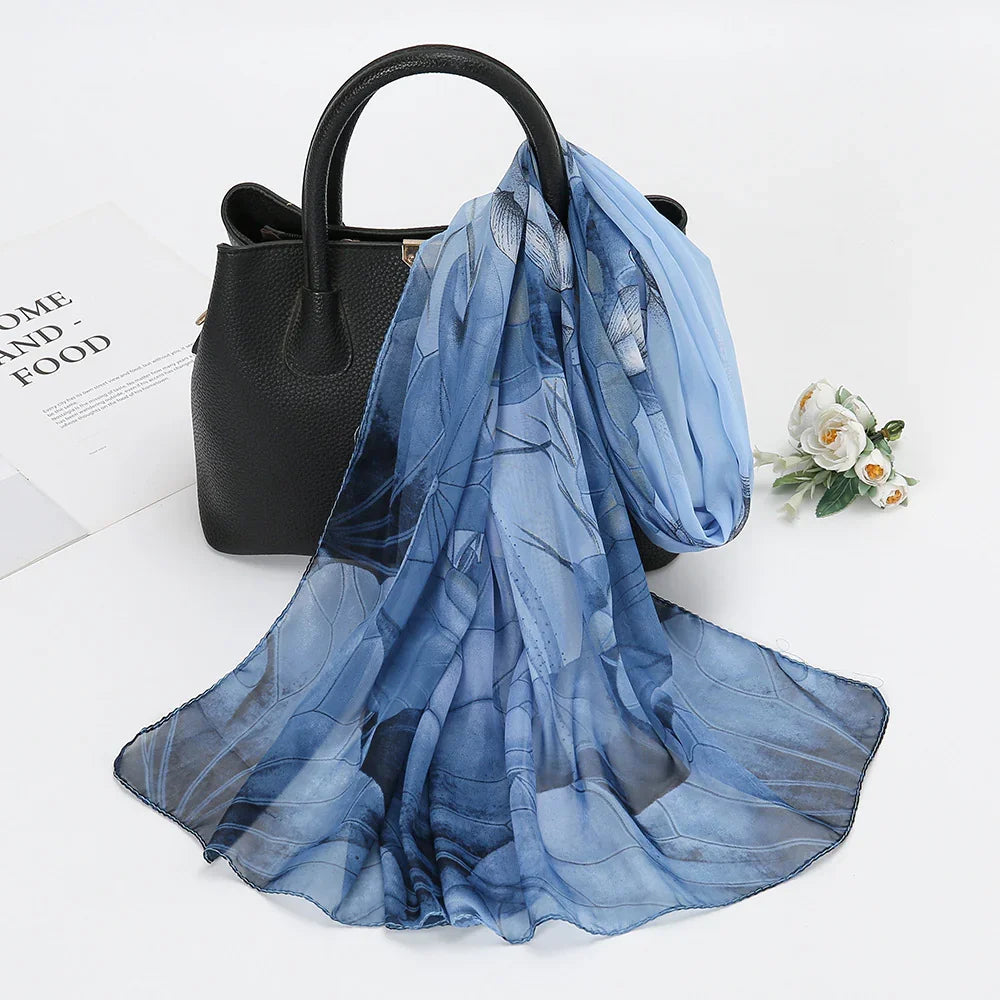 Black leather handbag with floral blue silk scarf draped over it on white surface with white roses