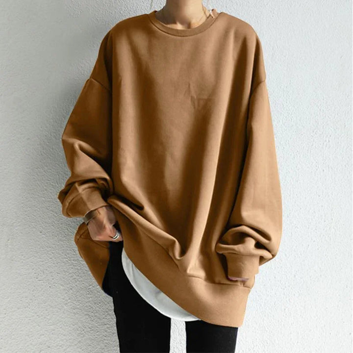 Person wearing oversized brown sweatshirt with white shirt layered underneath against white wall