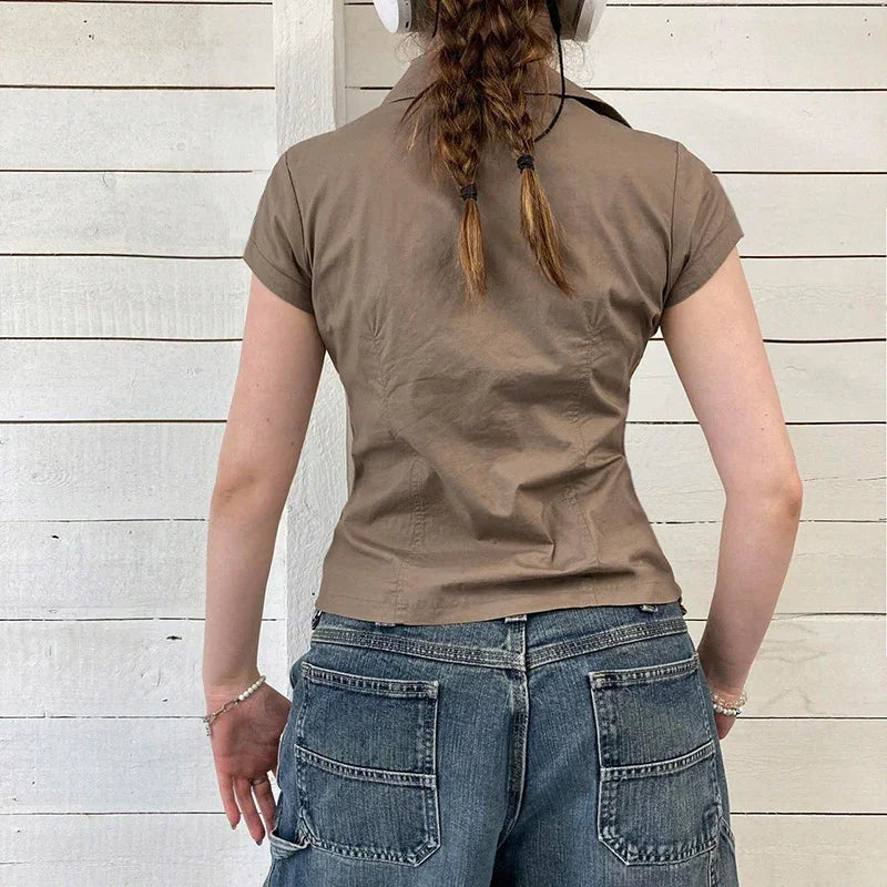 Woman with braided hair wearing short-sleeve brown shirt and blue denim jeans standing against white wooden wall