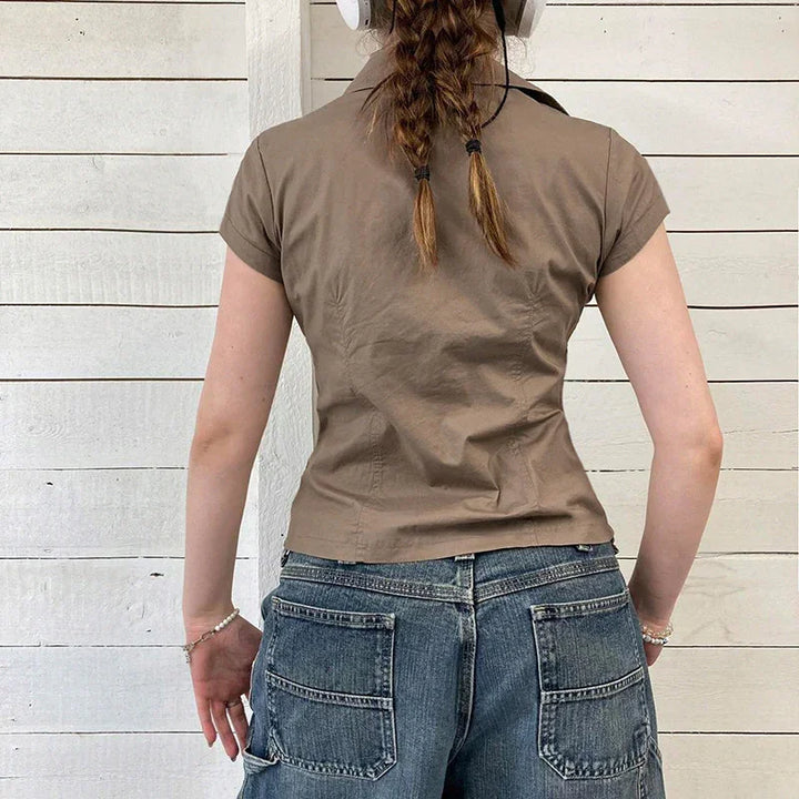 Woman with braided hair wearing short-sleeve brown shirt and blue denim jeans standing against white wooden wall