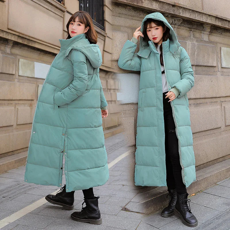 Woman modeling long teal puffer coat with hood, black boots, urban street background