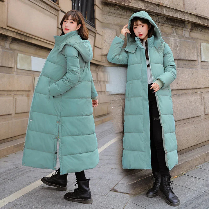 Woman modeling long teal puffer coat with hood, black boots, urban street background