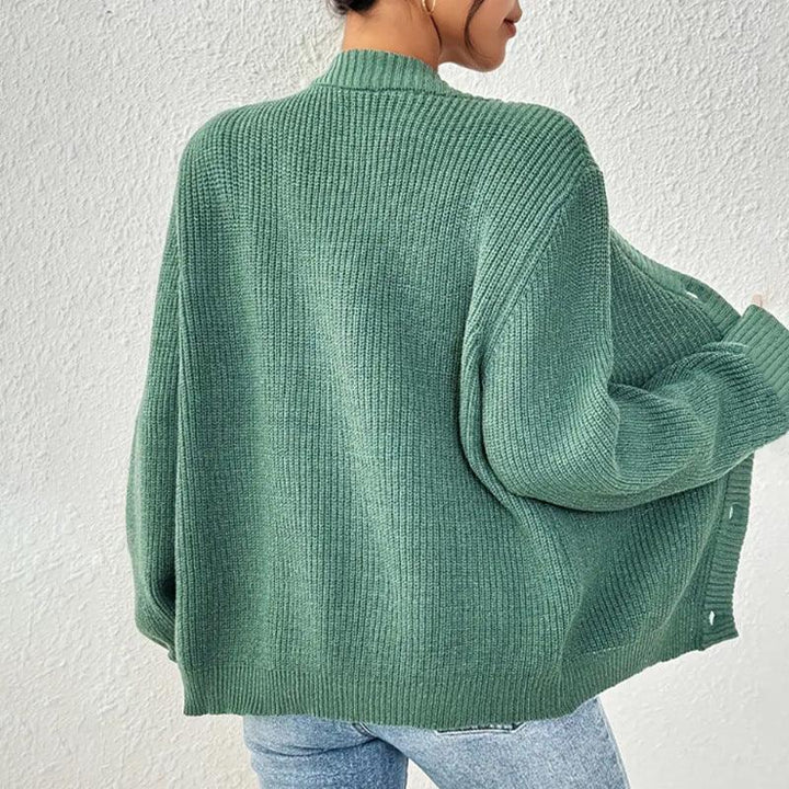 Woman wearing oversized sage green ribbed knit cardigan with jeans against white textured wall
