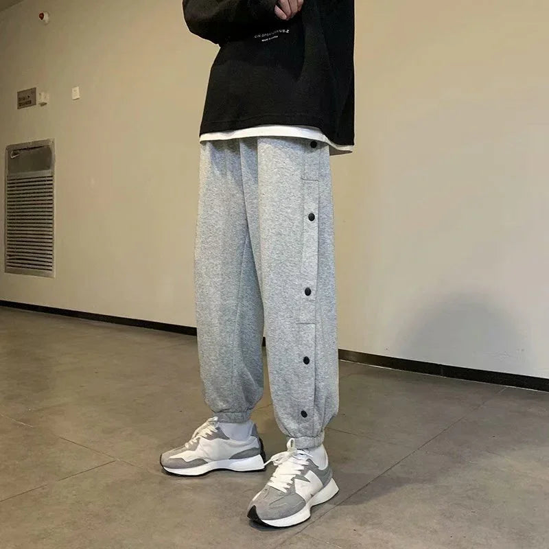 Person wearing gray jogger pants with black buttons and white sneakers in minimalist indoor setting