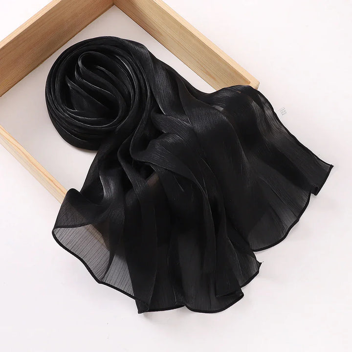 Black sheer chiffon scarf with subtle texture displayed on a light wooden tray