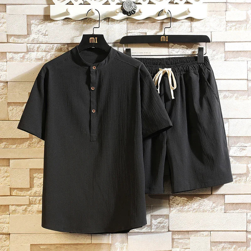 Black short-sleeve henley shirt and elastic waist shorts set hanging on black hangers against beige brick wall