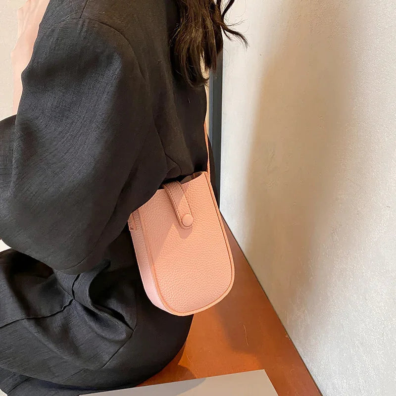 Woman wearing black dress sitting on wooden bench with small pink leather crossbody bag
