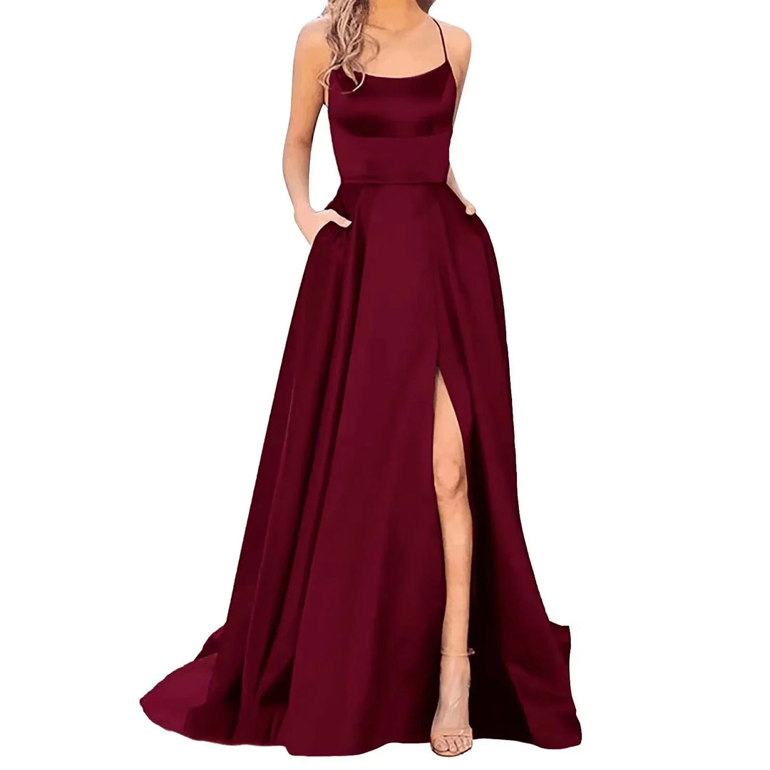 Elegant burgundy evening gown with spaghetti straps and thigh-high slit, styled with hands in pockets