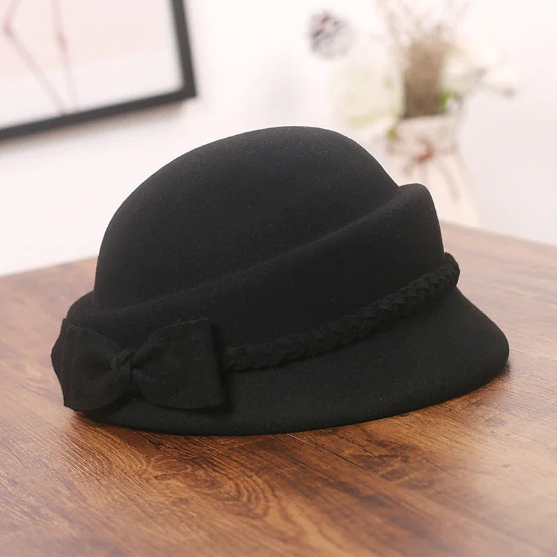 Black felt cloche hat with braided band and bow detail on wooden surface