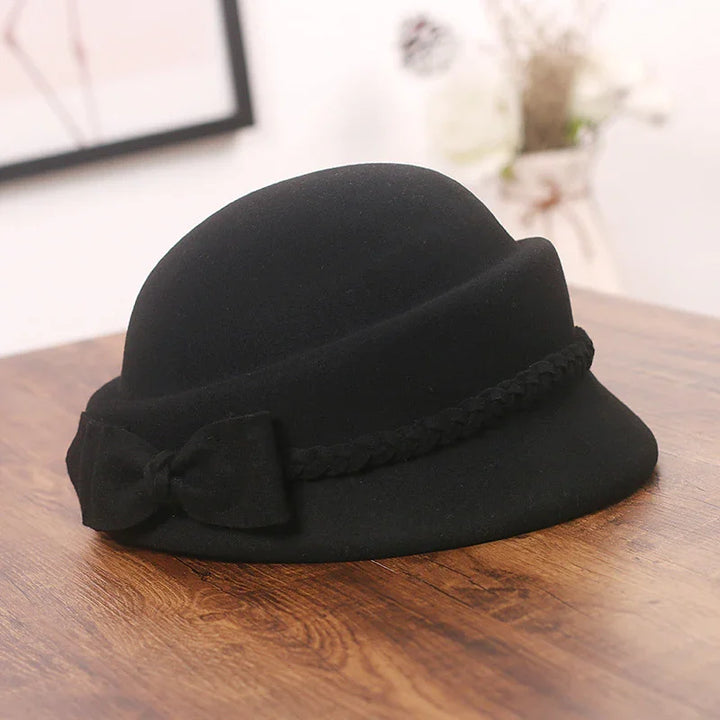 Black felt cloche hat with braided band and bow detail on wooden surface