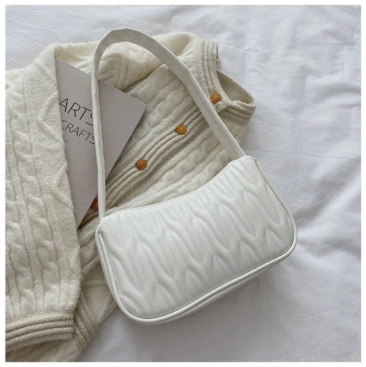 White quilted shoulder bag placed on cream cable knit cardigan with wooden buttons and a book