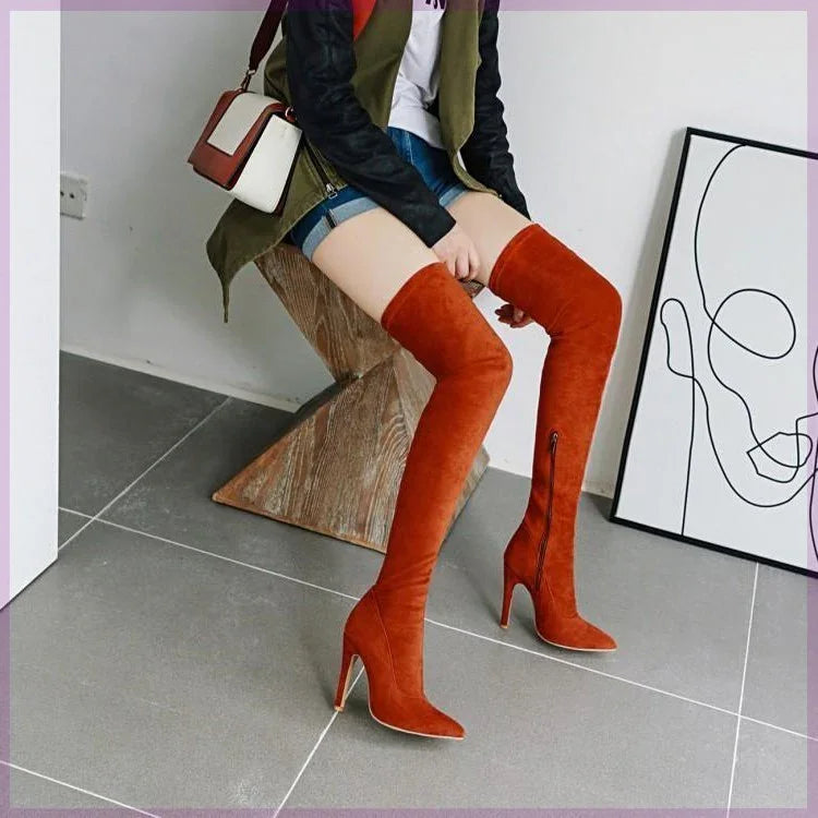 Woman sitting on wooden chair wearing rust orange suede over-the-knee high heel boots with zipper