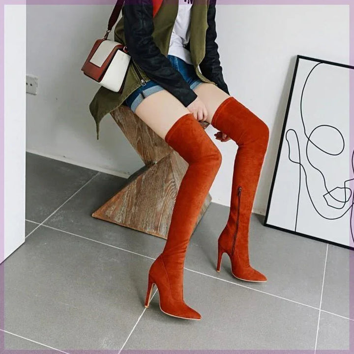 Woman sitting on wooden chair wearing rust orange suede over-the-knee high heel boots with zipper