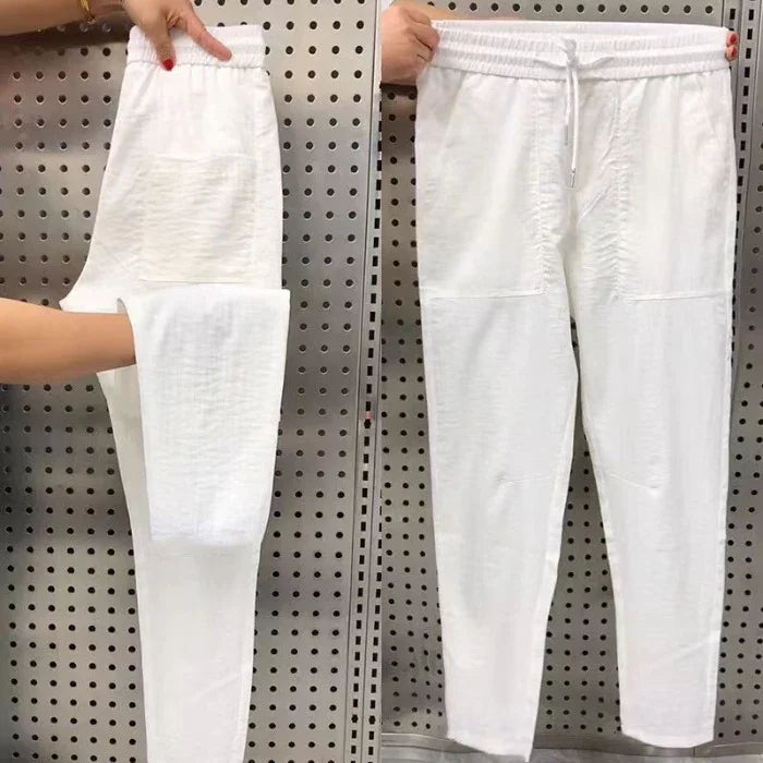 Hands holding white casual jogger pants with elastic waistband, drawstring, and front pockets against perforated gray wall