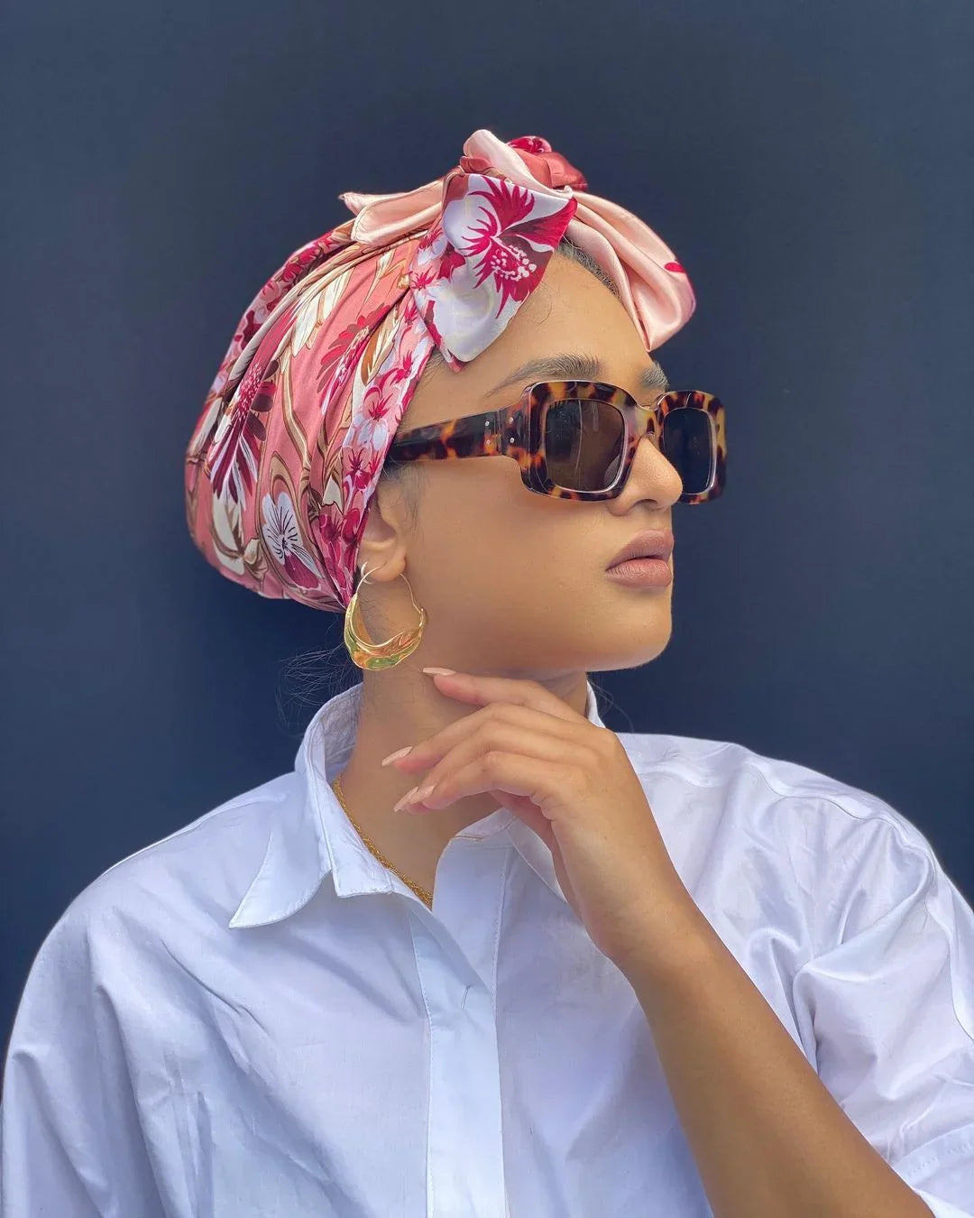 Woman wearing tortoiseshell sunglasses, floral pink headscarf, gold hoop earrings, and white shirt