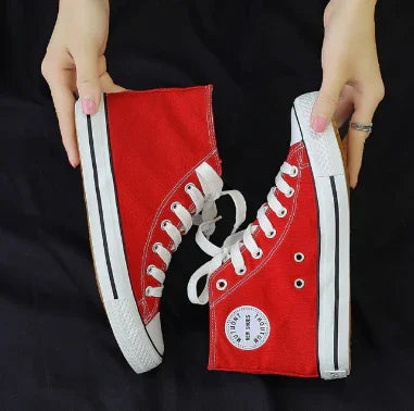 Hands holding red high-top canvas sneakers with white laces and rubber soles on black background