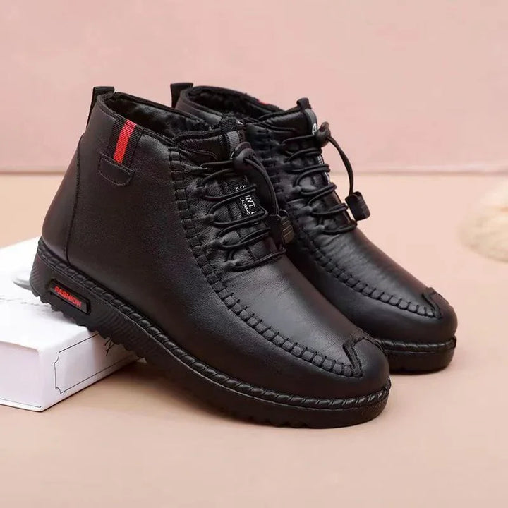 Black leather casual ankle boots with decorative stitching and red stripe detail on beige background