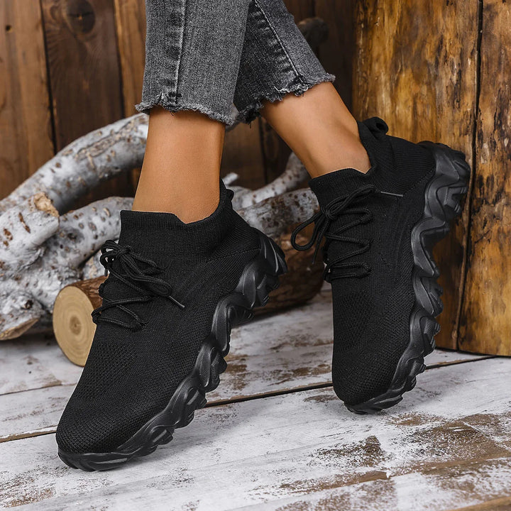 Black knit sock sneakers with chunky sole worn with frayed gray jeans on rustic wooden floor