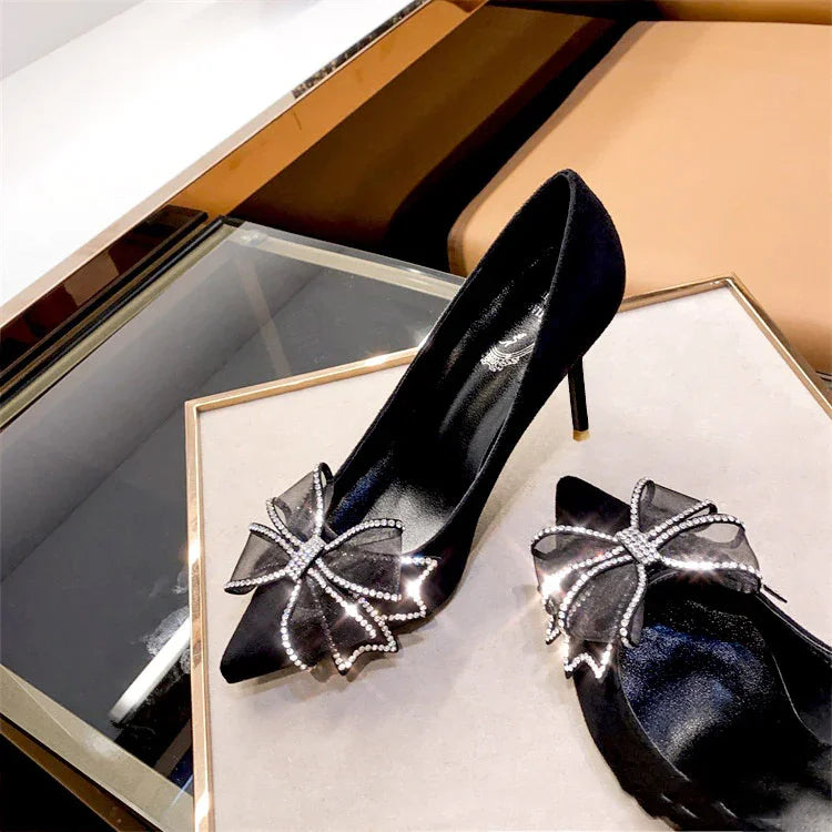 Elegant black high-heeled shoes with sparkling rhinestone bow decoration on a display table