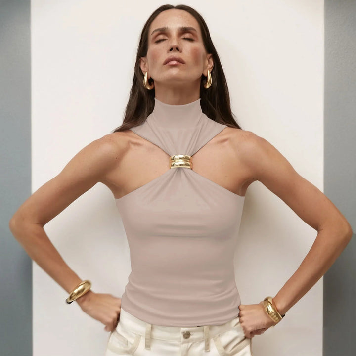 Woman wearing beige halter top with gold ring detail and gold jewelry posing with eyes closed