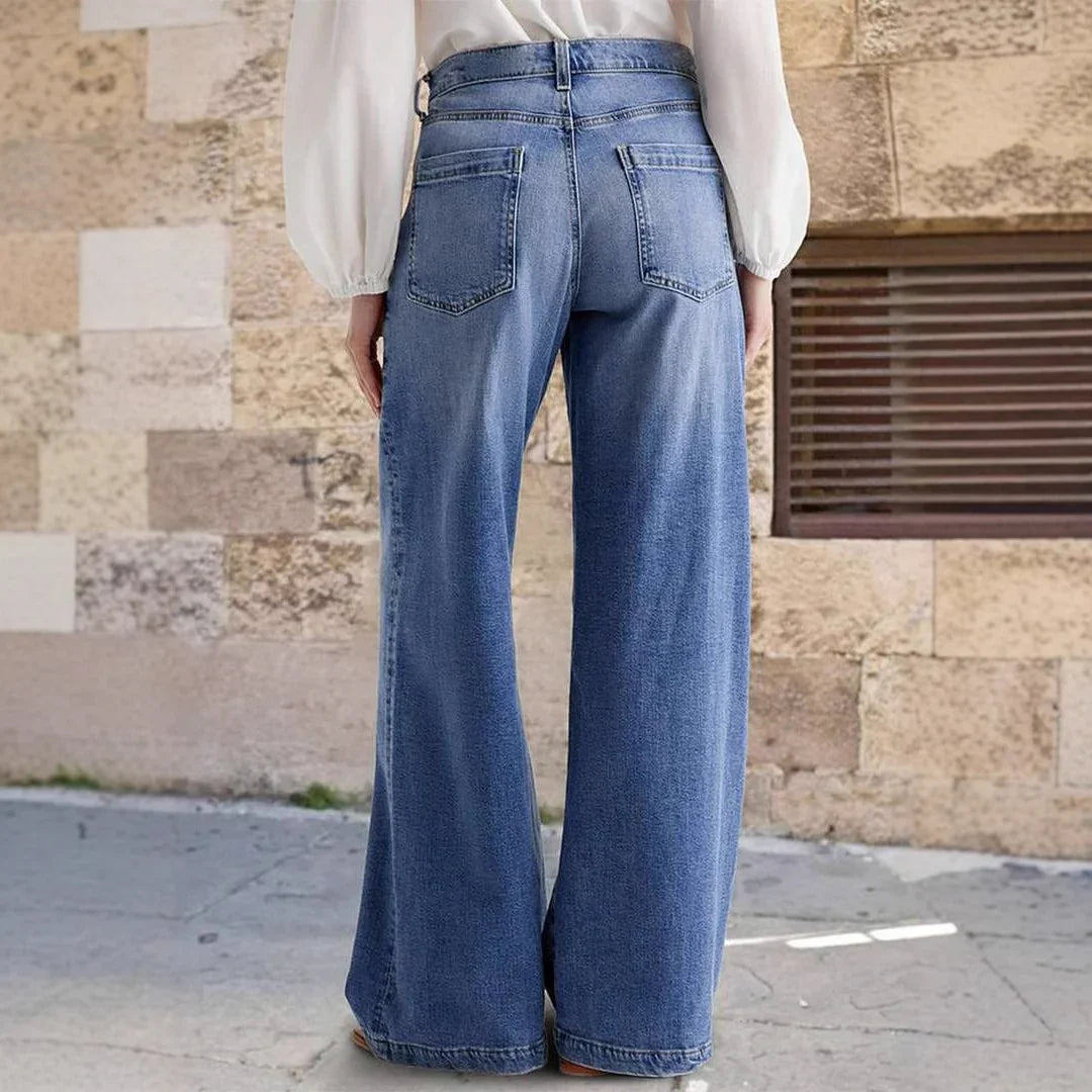 Woman wearing high-waisted wide-leg blue denim jeans outdoors against a stone wall