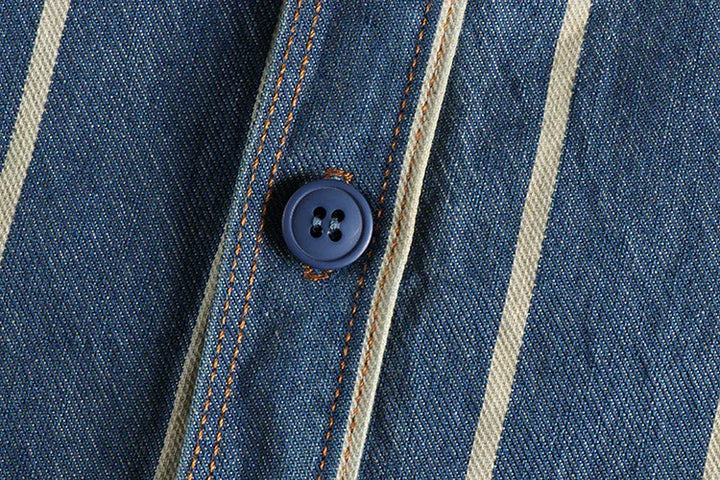 Close-up of denim fabric with cream stripes and a navy blue button secured with orange thread