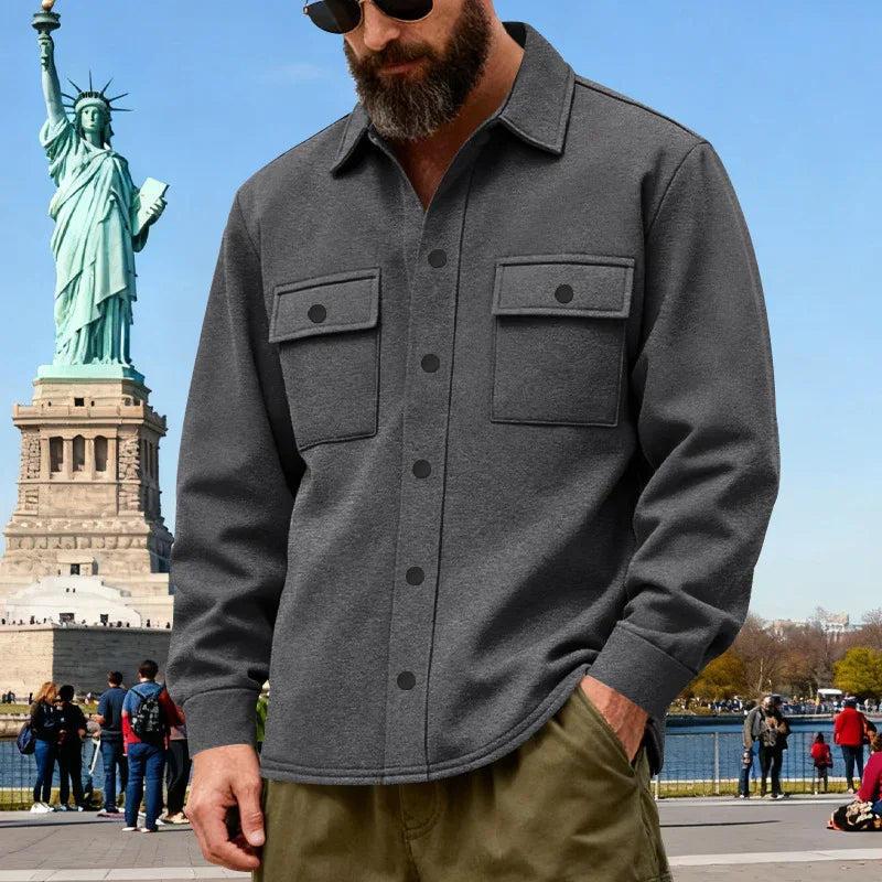 Man wearing dark gray button-up shirt with chest pockets near Statue of Liberty on a sunny day