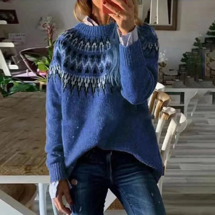 Woman wearing blue patterned knit sweater and jeans taking mirror selfie in cozy dining room