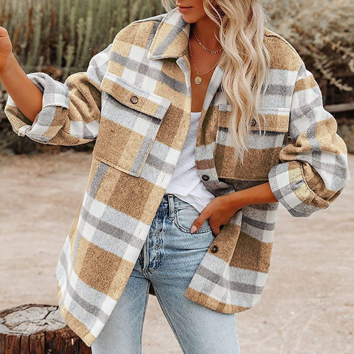 Woman wearing beige and gray plaid shacket with rolled sleeves, white top, and light blue jeans outdoors