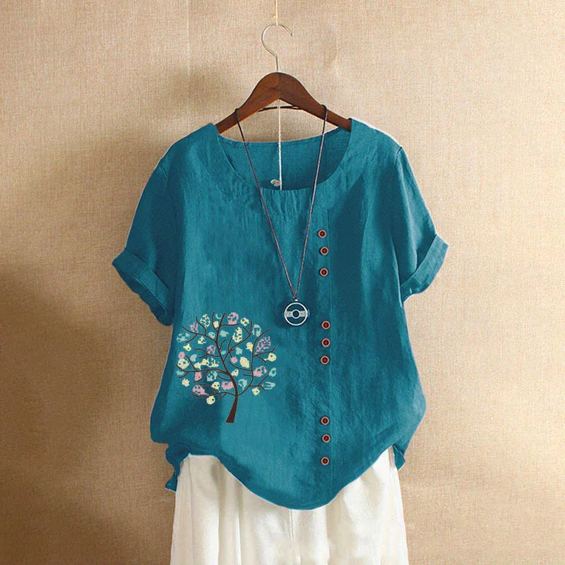 Blue short-sleeve blouse with floral tree print and button details on wooden hanger