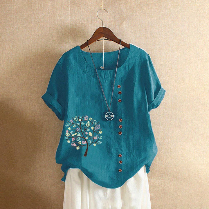 Blue short-sleeve blouse with floral tree print and button details on wooden hanger
