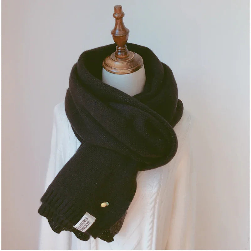 Black cozy knit scarf with pineapple pin and label, styled on a white mannequin with wooden neck stand