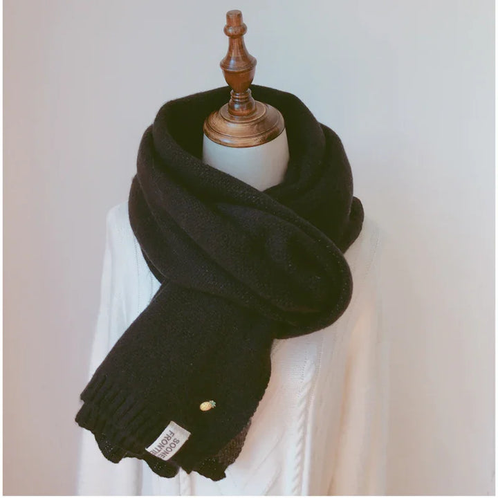 Black cozy knit scarf with pineapple pin and label, styled on a white mannequin with wooden neck stand