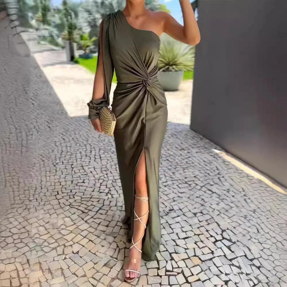 Woman wearing elegant olive green one-shoulder dress with thigh slit, holding gold clutch on cobblestone path