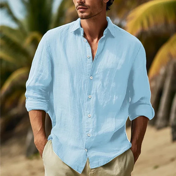 Man wearing light blue linen shirt and beige pants on a beach with palm trees