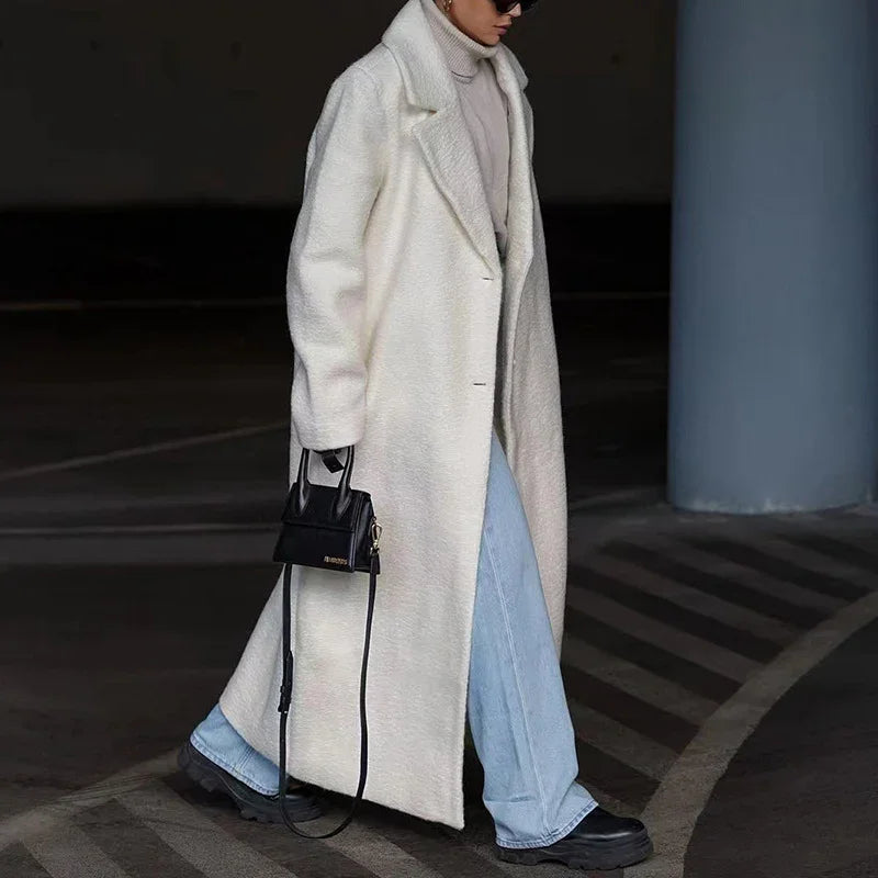 Woman in a long white fuzzy coat, light blue jeans, black chunky shoes, and black handbag walking in urban setting
