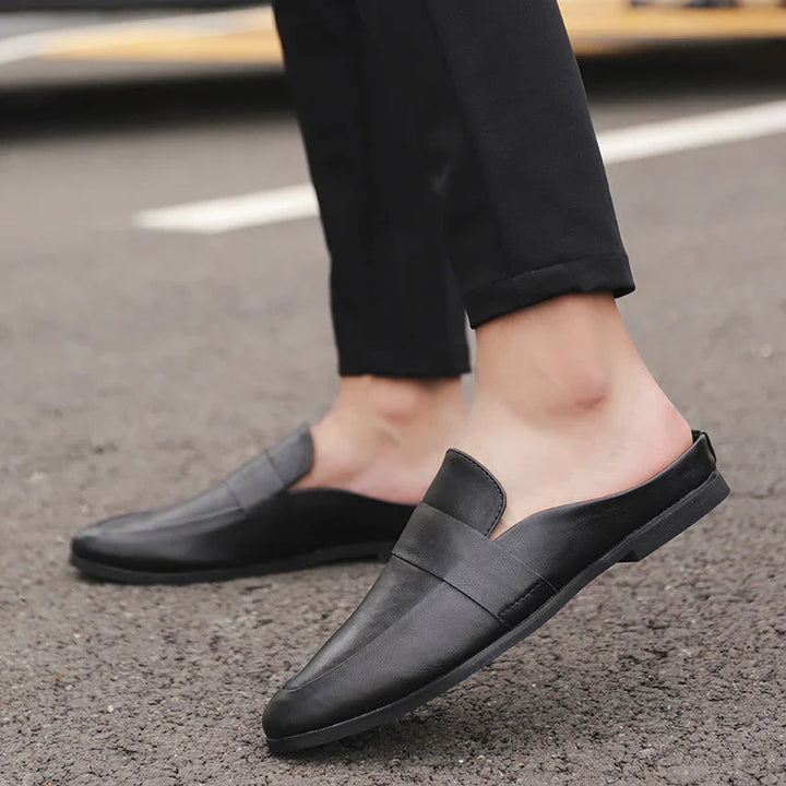 Person wearing black leather slip-on loafers with backless heel on asphalt road