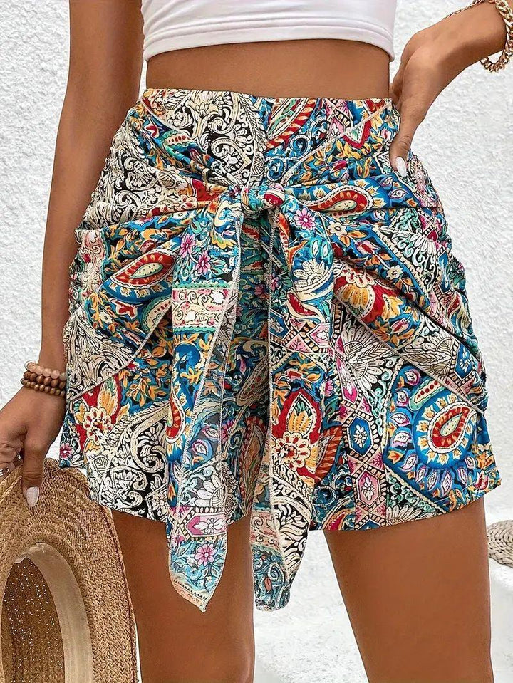 Woman wearing colorful boho print high-waisted shorts with tie front and holding a straw hat
