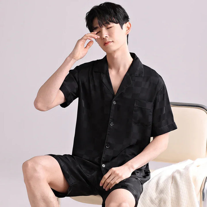 Young man in black checkered short-sleeve pajama set sitting on beige chair