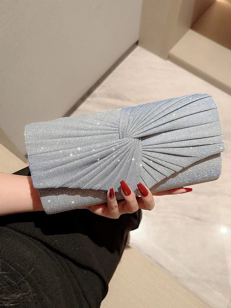 Hand holding silver glittery clutch purse with pleated design and red manicured nails