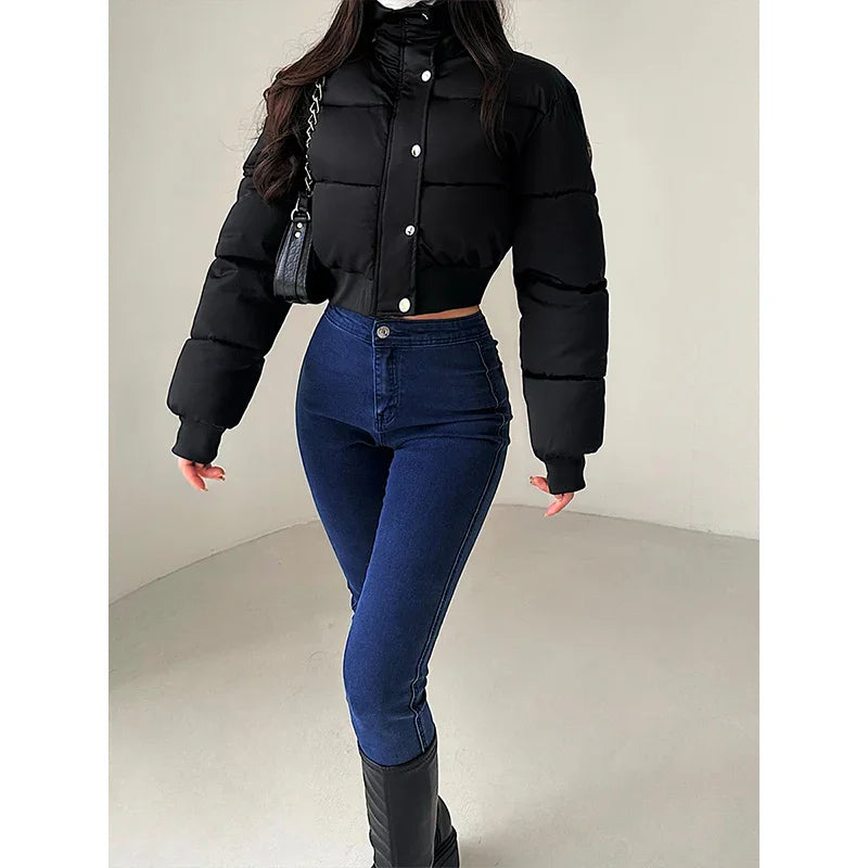 Woman wearing black cropped puffer jacket, high-waisted skinny blue jeans, and black boots in minimal indoor setting