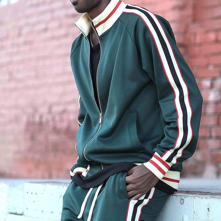 Man wearing green track jacket and pants with white and red stripes, brick wall background