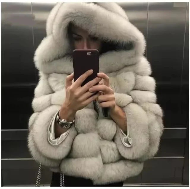 Person wearing a thick white fur coat with a large hood taking a mirror selfie in an elevator
