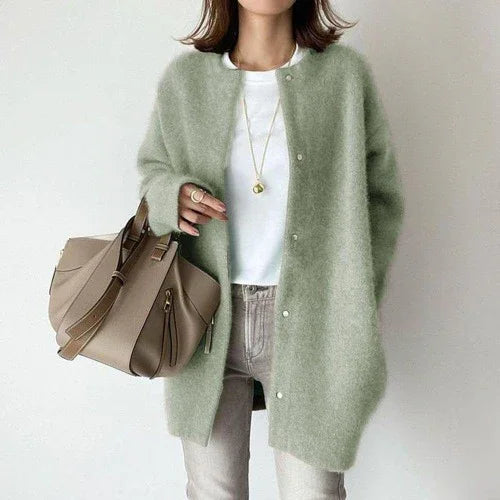 woman wearing light green fuzzy cardigan over white shirt with beige handbag and gray pants